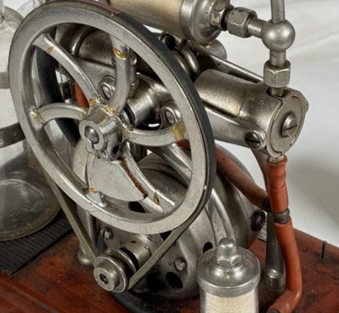 Figure 2 — The belt path, seen from the drive side: the small stepped motor pulley at lower left, the belt rising to the flywheel rim, and the pump crankcase behind with its ring of ventilation openings.