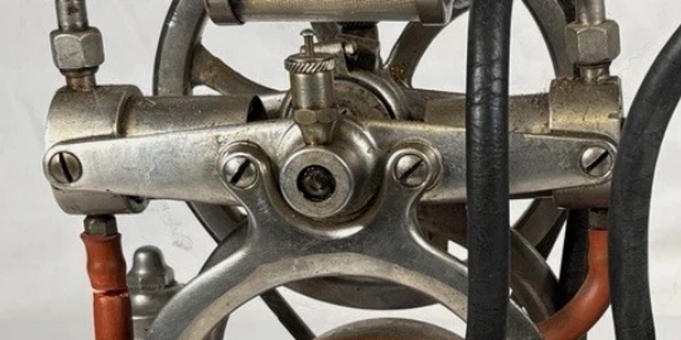 Figure 4 — The pump head, with the knurled adjuster on its spring-loaded stem at centre — the pressure control. The two horizontal cylinders sit in split clamps either side; the machine number is stamped into…