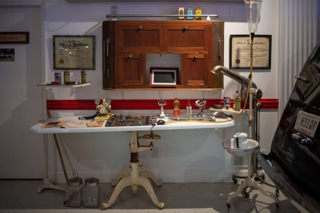 Figure 3 — A mid-century mortuary preparation room preserved as a museum tableau: the porcelain table, the injection machine on its stand, and cabinetry — equipment only.
