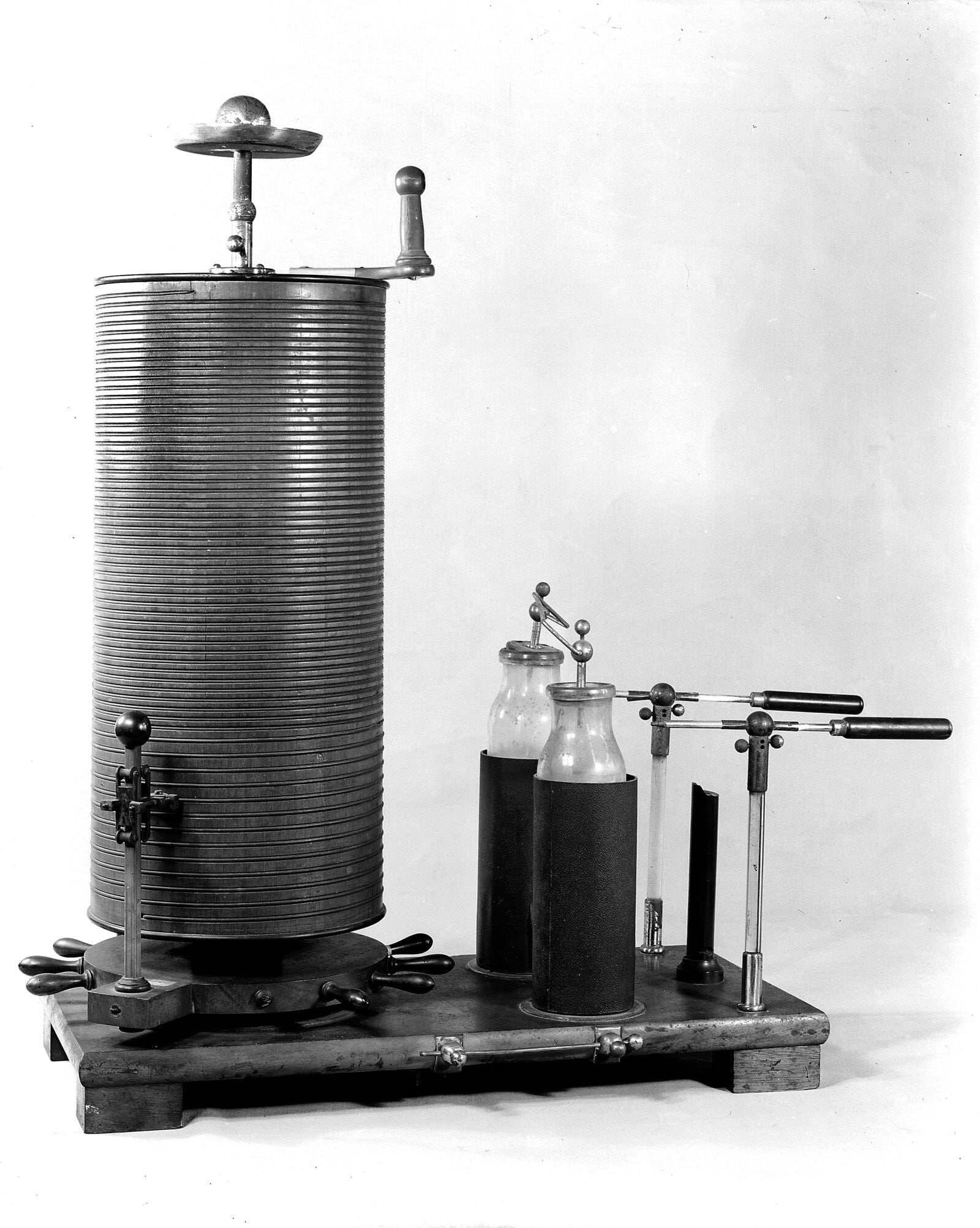Figure 2 — An Oudin-type resonator: the tall close-wound secondary standing on its base with the discharge terminal above, and beside it the Leyden jars and electrode handles that completed the outfit. Photog…