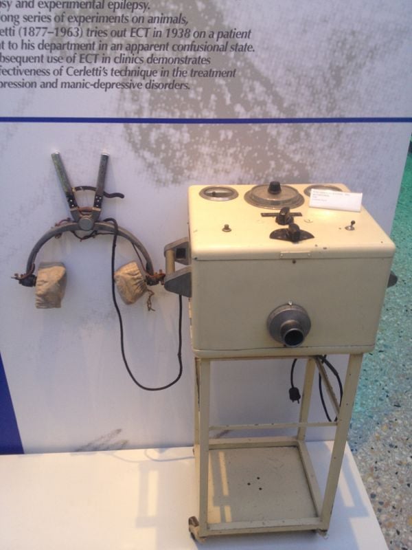 Figure 2 — A Cerletti electroshock apparatus preserved in a museum display, with its head electrode carrier on the stand beside the control box. The object is presented here as a historical document and nothi…