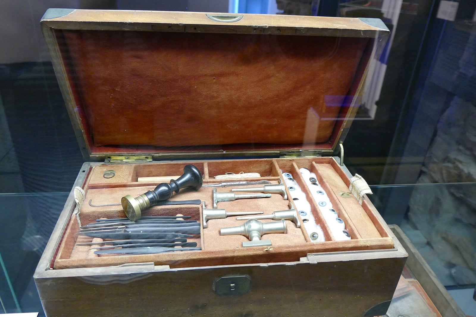 Figure 2 — A cased embalming outfit in the Museum für Sepulkralkultur, Kassel — instruments and glass bedded in a fitted wooden case. The case is the era's whole logic: the trade travelled to the house, so th…