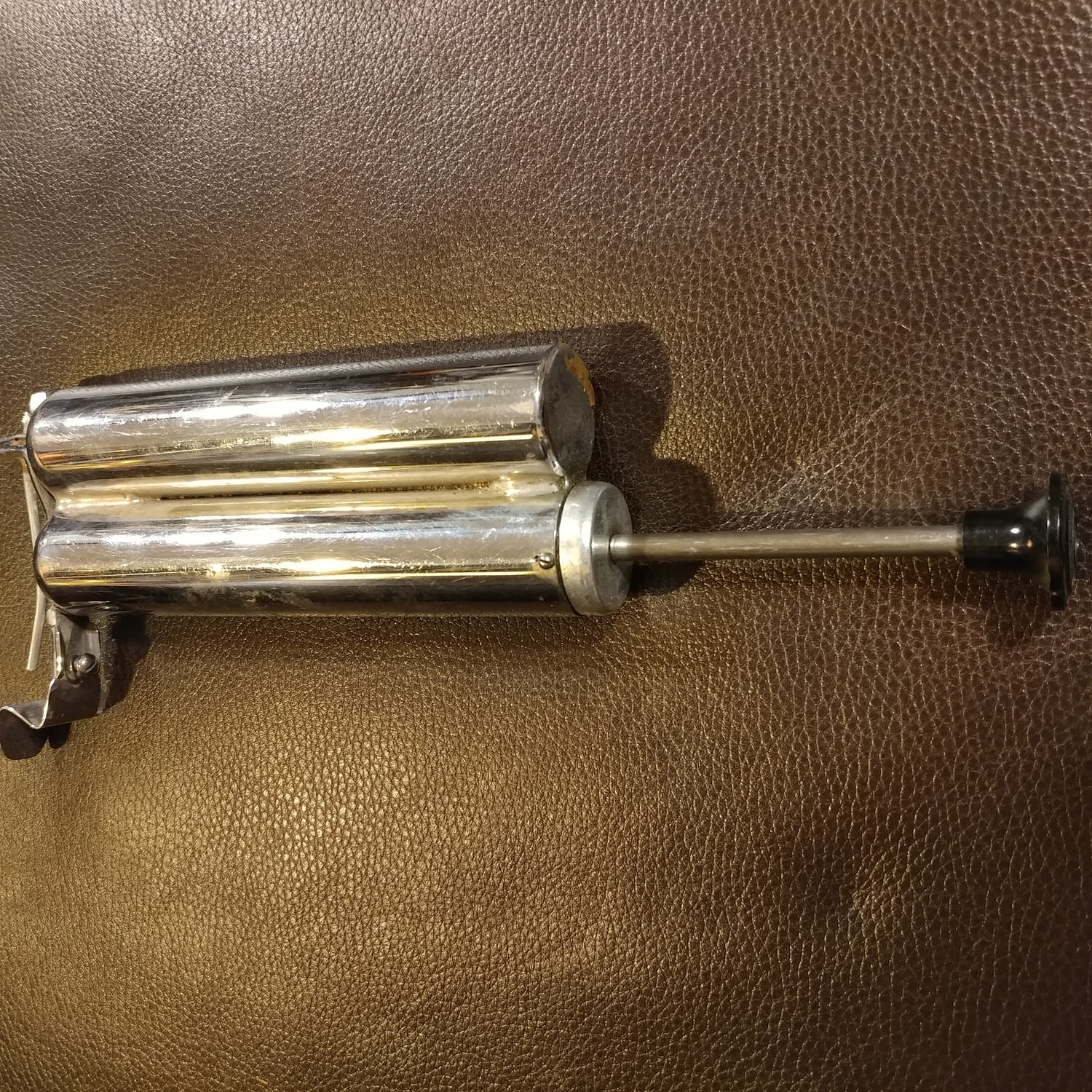 Figure 3 — A nickel-plated piston hand pump from a portable outfit: the barrel, the drawn-out plunger with its thumb rest, and the finger grips brazed to the body so one hand could hold and pump. Everything t…