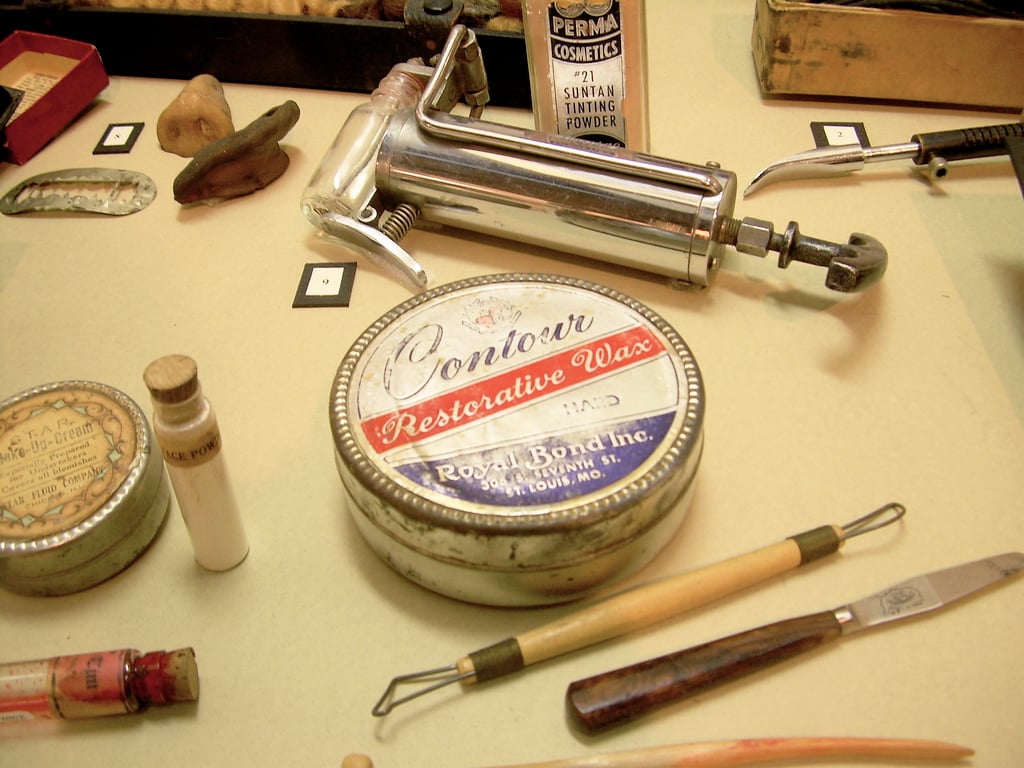 Figure 6 — The shop's smaller goods laid out in a museum case: a nickel-plated hand injector, a tin of Contour Restorative Wax, tinting powder and modelling tools. The machines get the attention, but this is …