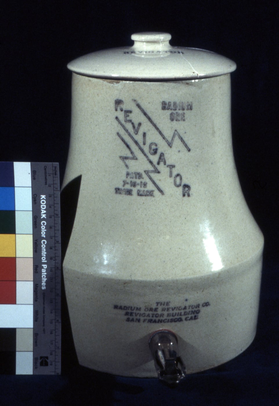Figure 2 — A radium-ore Revigator water crock with its spigot — the carnotite-lined stoneware that a surveyor reads at a few mR/hr and that leached radon plus arsenic, lead, and uranium into the "revigated" w…