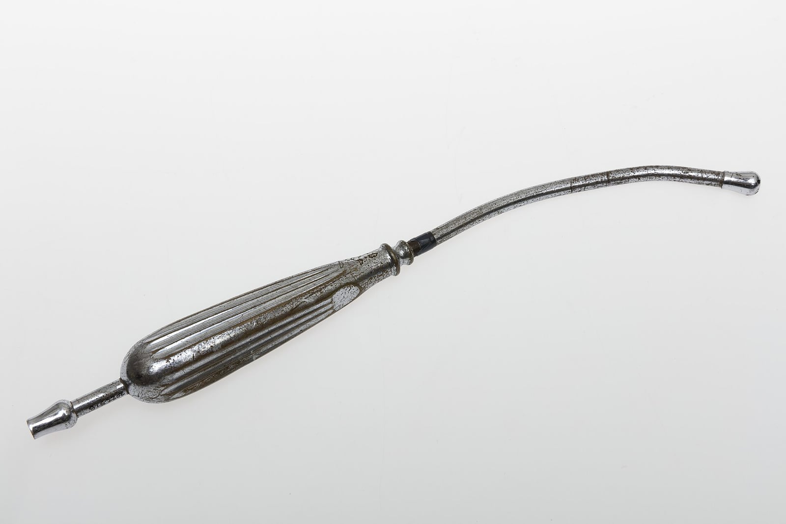 Figure 3 — The original as it was made: a reusable metal Yankauer suction tube, the bulbous fenestrated head at one end and a fluted handle at the other. This one belonged to Dr. John Hersel Gladney. Set it b…