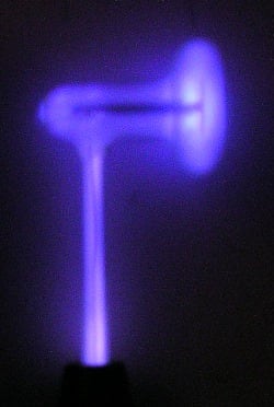 Figure 2 — A single glass electrode lit in the hand, the residual gas inside glowing violet — a low-pressure gas discharge, not an ultraviolet beam.